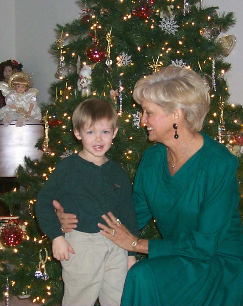 Ashton as a small boy in a green sweater and khakis, standing at the Christmas tree with his Grandmother Love in festive green
