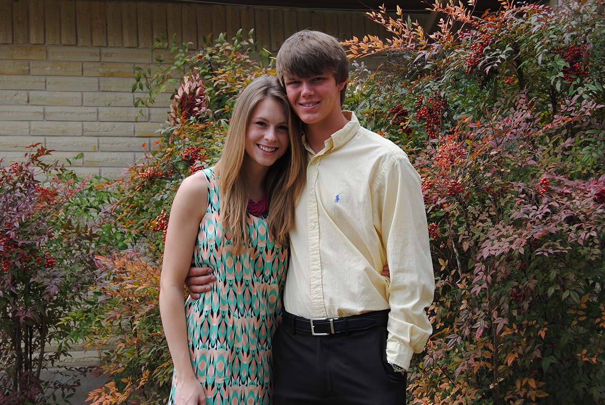 Ashton dressed up in a pale yellow button-down with his girlfriend against autumn foliage — dance or homecoming night