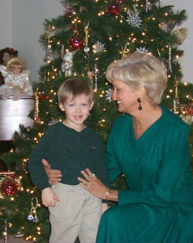 Ashton as a small boy in a green sweater and khakis, standing at the Christmas tree with his Grandmother Love in festive green