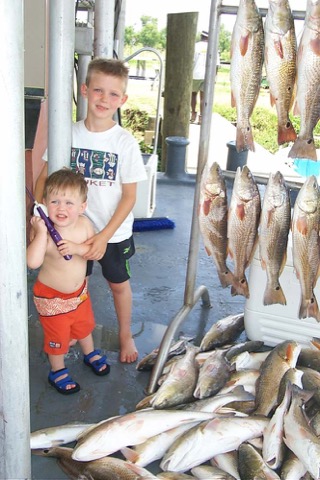 Two young boys at a dock beside an enormous day's catch of fish hung on the board and piled below