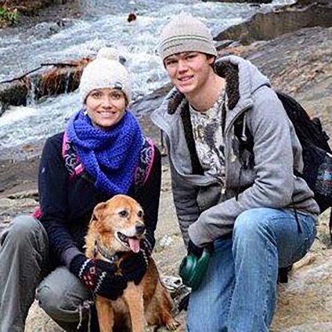 Winter hike on the rocks — Ashton in beanie and gray jacket crouched beside his Aunt Cayce and the golden dog, both smiling wide