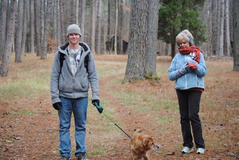Ashton in a gray hoodie and beanie walking his dog on a pine-woods trail, his Grandmother Love beside him cradling a fishing rod