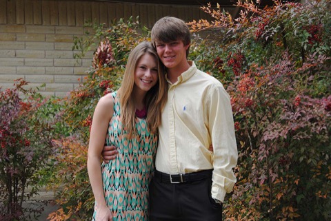 Ashton dressed up in a pale yellow button-down with his girlfriend against autumn foliage — dance or homecoming night